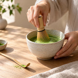 Fouet chasen battant du matcha vert dans un bol en céramique sur une table en bois